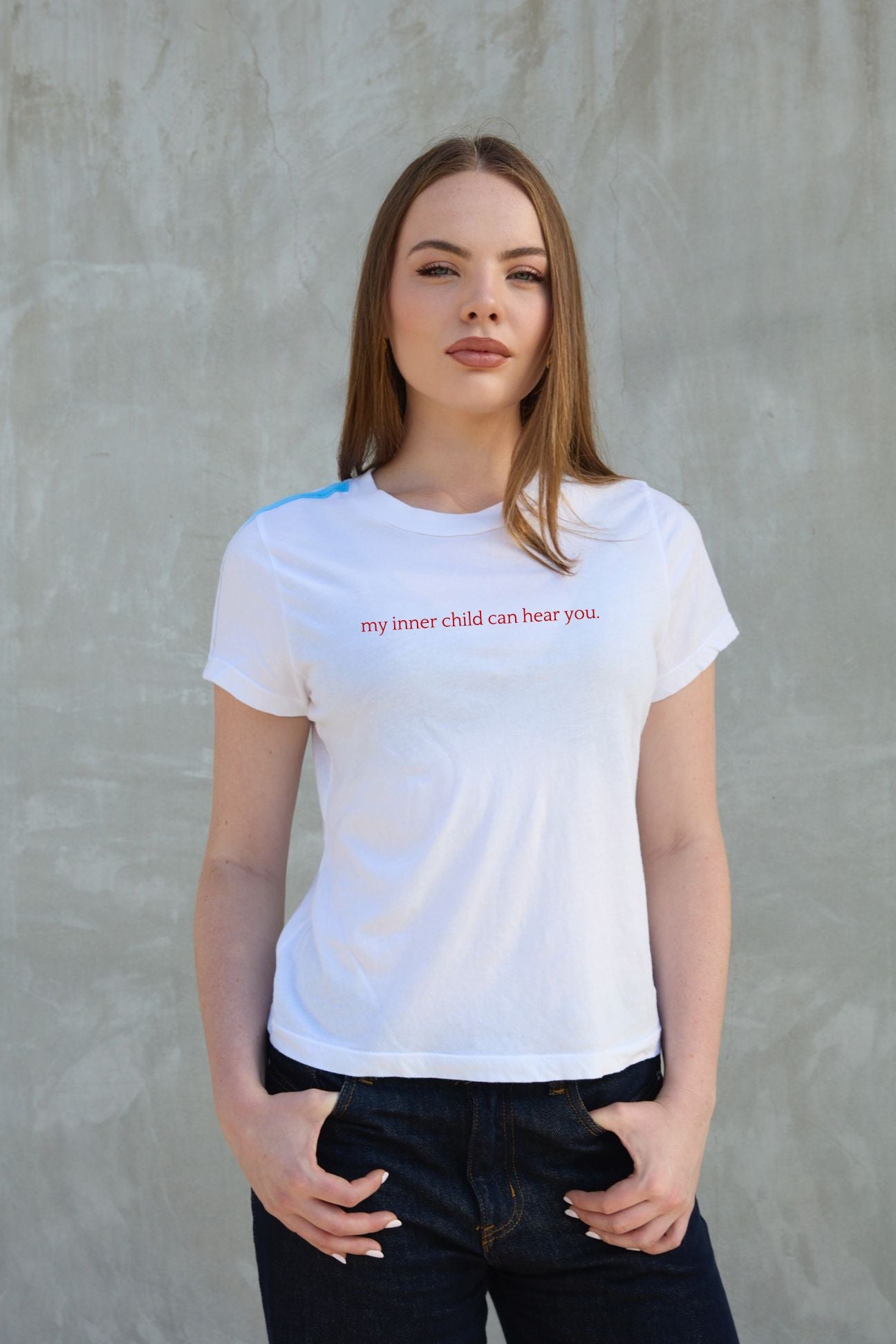 Woman wearing a white t-shirt with text against a gray concrete wall