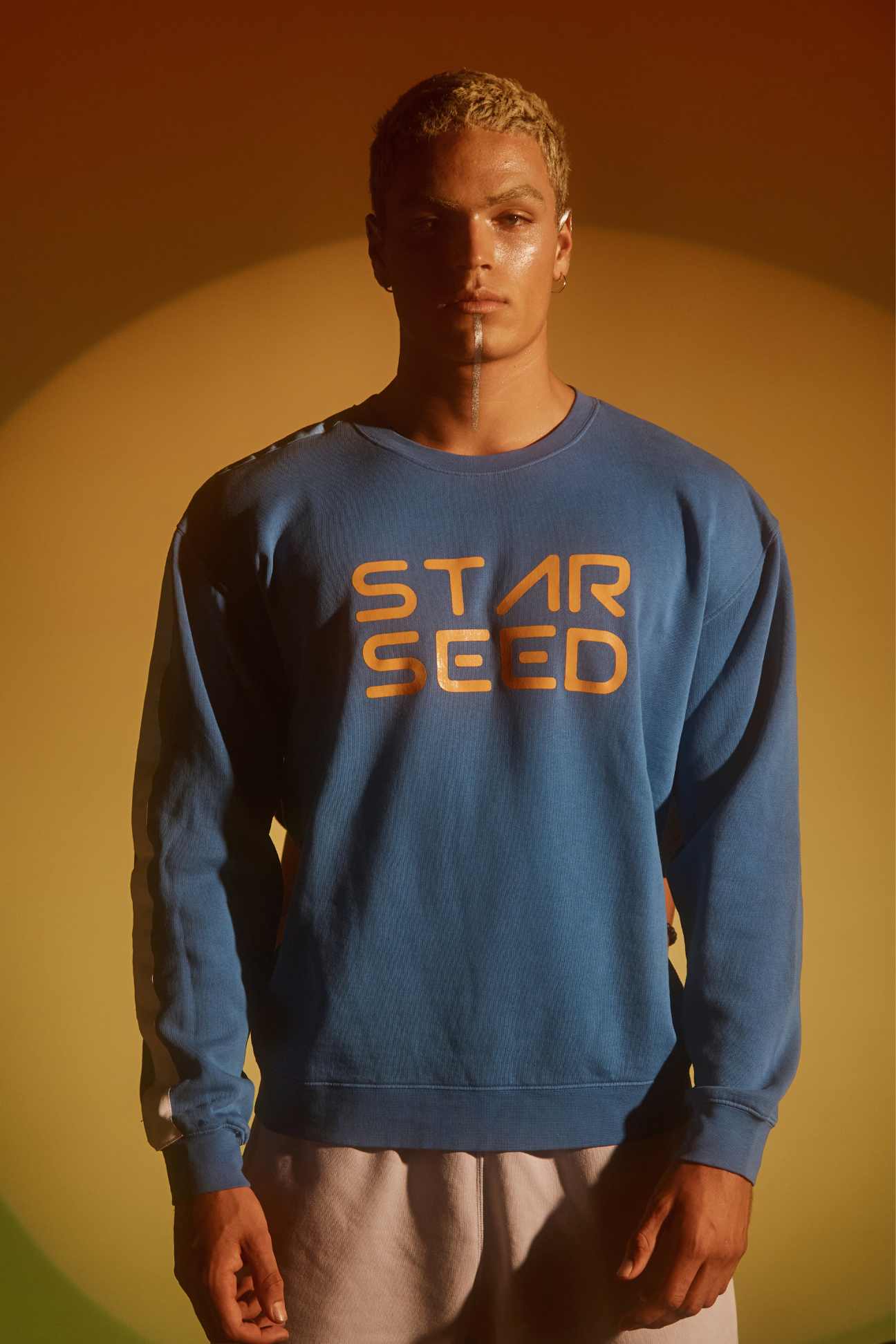 A male model wearing a blue sweatshirt with 'STAR SEED' written in orange text across the front.