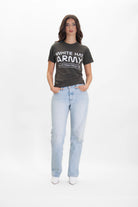 A woman stands against a white background, wearing a White Hat Army Tee in Caladan by GFLApparel that reads "WHITE HAT ARMY" in bold statement print, paired with light blue jeans and her hands in her pockets.