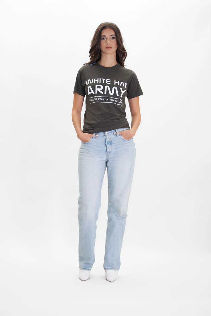 A woman stands against a white background, wearing a White Hat Army Tee in Caladan by GFLApparel that reads "WHITE HAT ARMY" in bold statement print, paired with light blue jeans and her hands in her pockets.