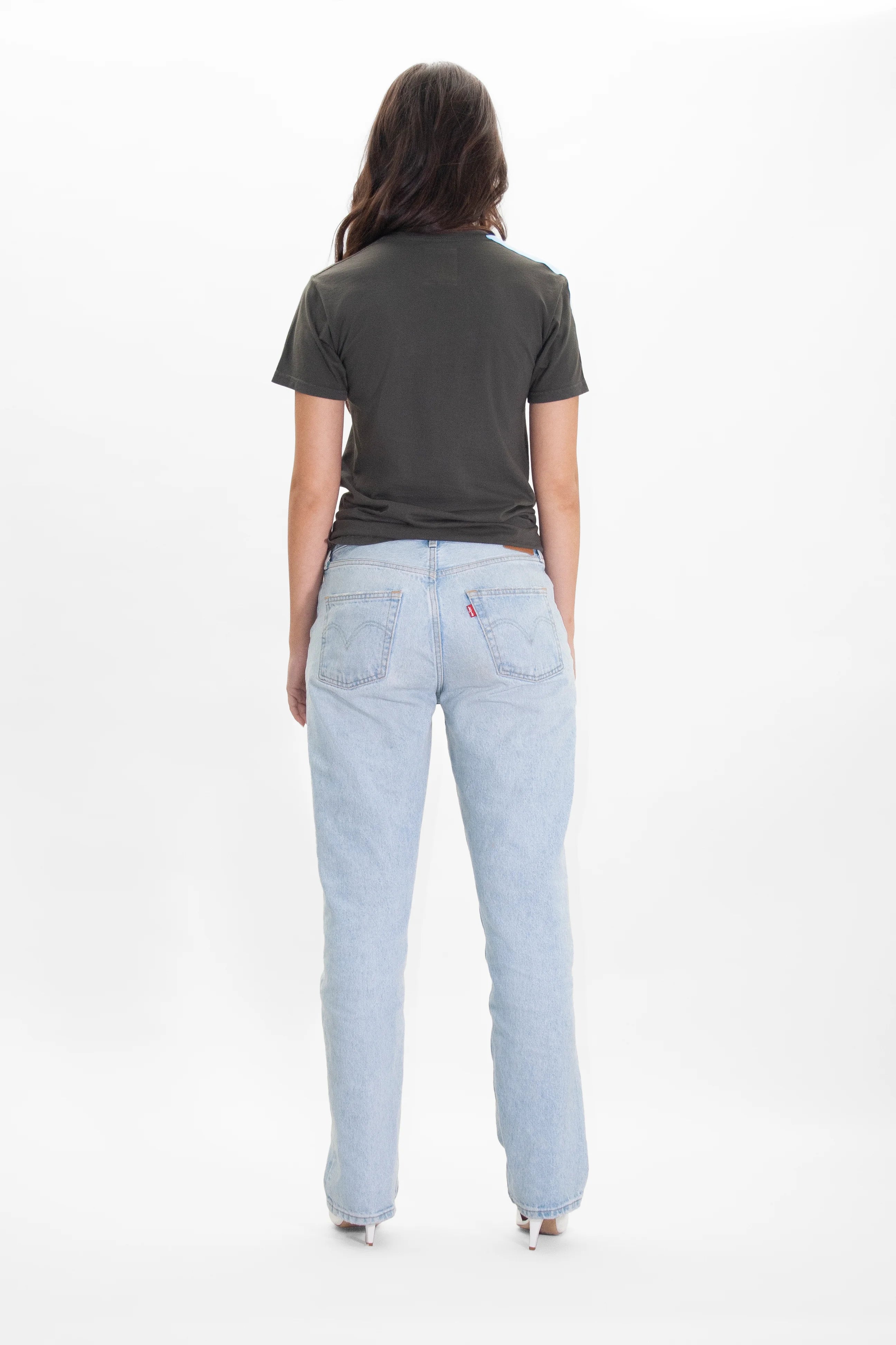 A person with long hair is standing with their back facing the camera, wearing a White Hat Army Tee in Caladan by GFLApparel and light blue jeans.