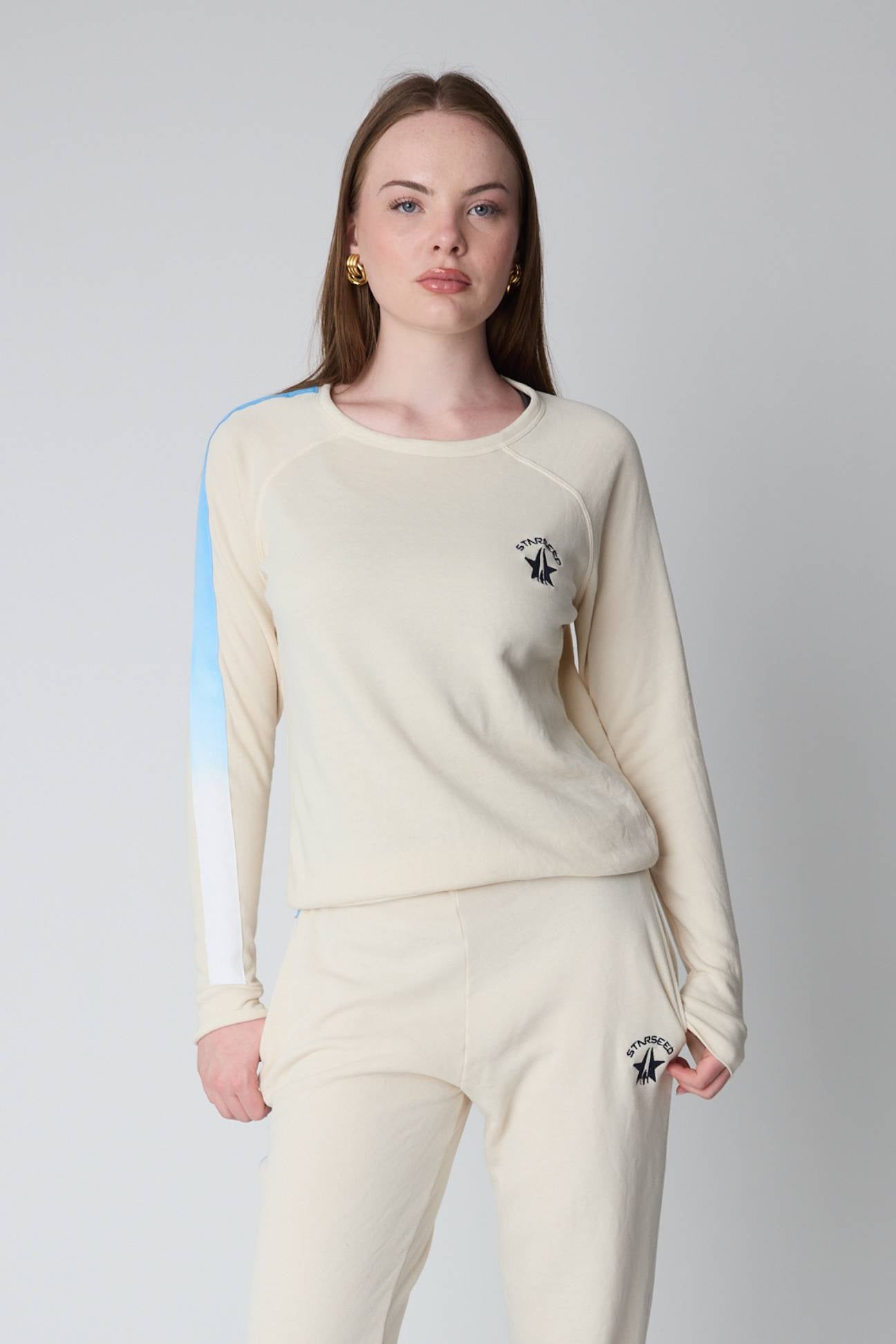 Woman wearing a cream-colored outfit with a logo on a plain background
