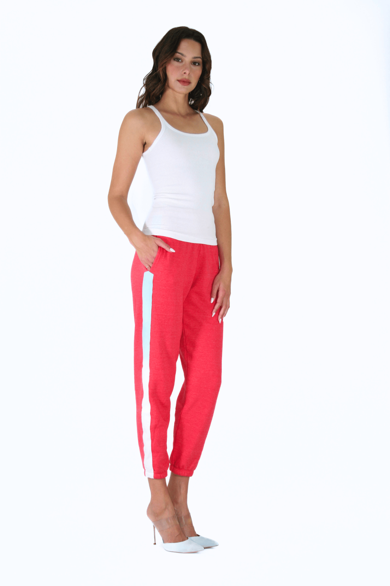 Woman standing in white tank top and red Angel Number 444 track pants with white stripes, embodying the divine intention of her guardian angels.