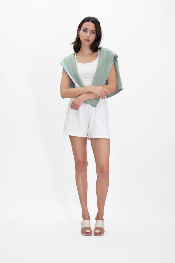 A woman wearing the Angel Number 1111 Cropped Tank in Bone by GFLApparel, along with white shorts and a green shawl.