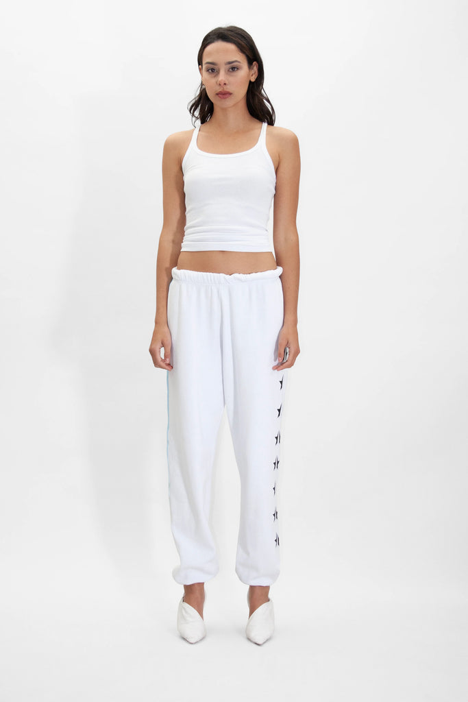 A woman in a white tank top and GFLApparel GFL Stars Sweatpants in Lite Beam stands against a plain white background, wearing matching white shoes.