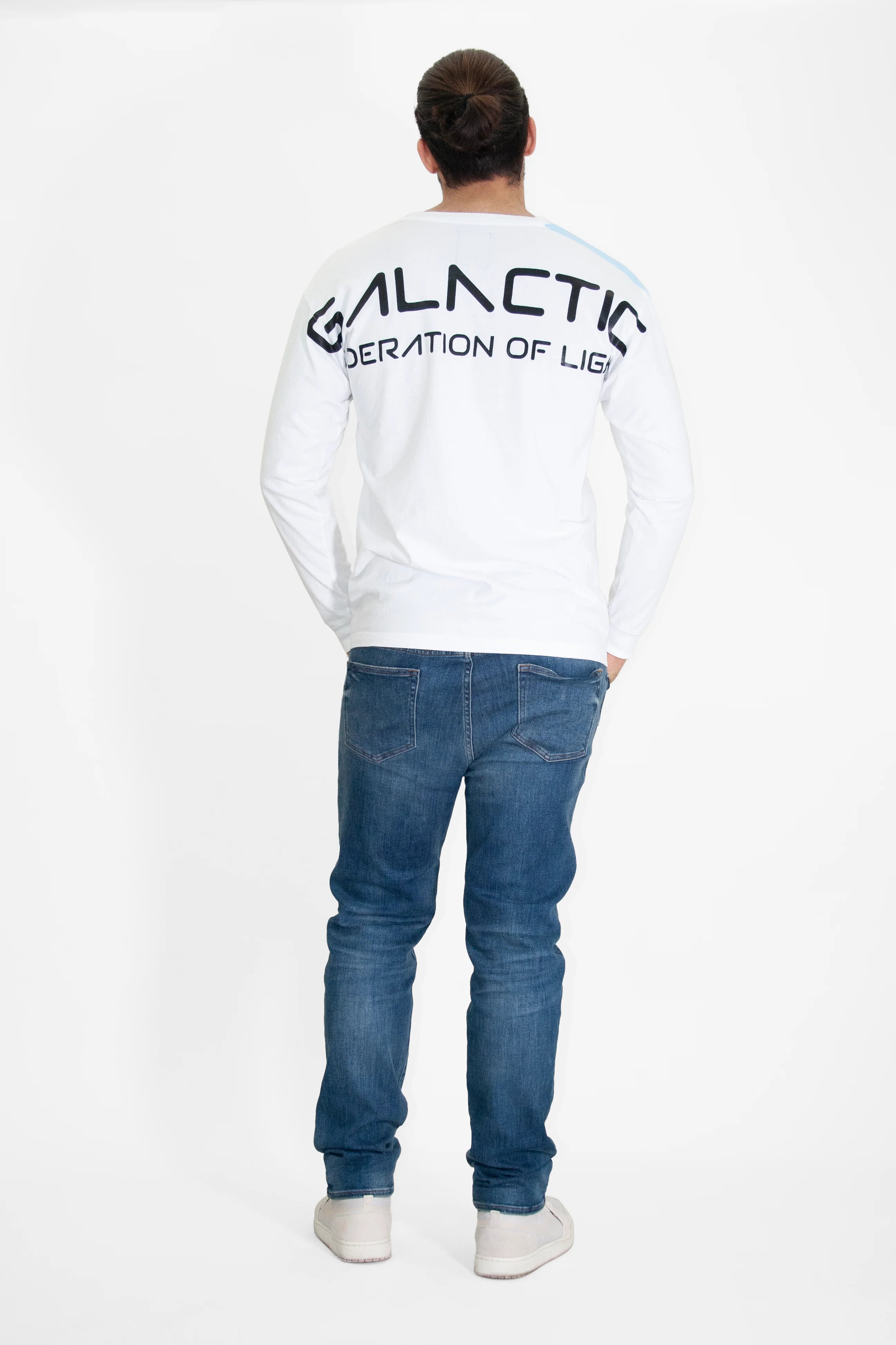 A person with long hair in a bun wears a white long-sleeve shirt, the **GFL Stars L/S in Lite Beam** by **GFLApparel**, paired with blue jeans and white shoes, standing against a white background. Notably, their attire hints at an affiliation with the GFL Stars.