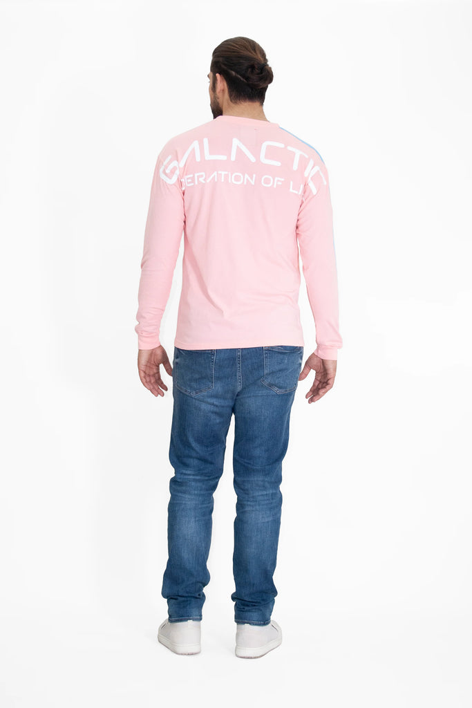 A man with a bun hairstyle is facing away from the camera, wearing a relaxed fit, long-sleeved GFLApparel GFL Stars L/S in Sun Fade with "GALACTIC GENERATION OF LIFE" printed on the back, blue jeans, and white sneakers made of breathable cotton.