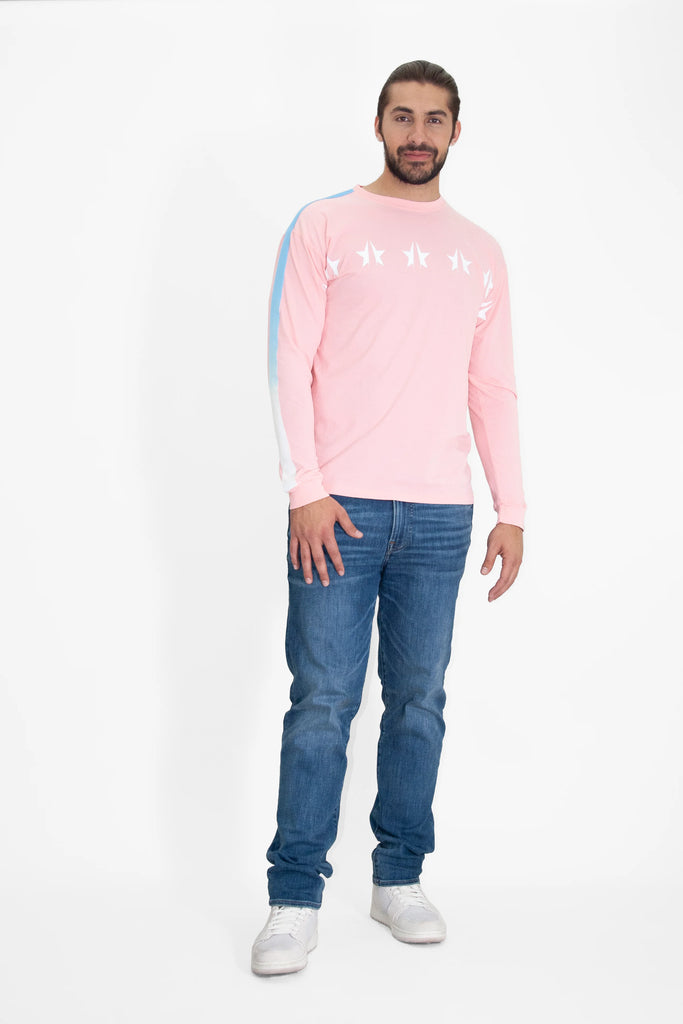 A man with long hair and a beard is wearing a relaxed fit, GFL Stars L/S in Sun Fade by GFLApparel, blue jeans, and white sneakers. He is standing against a plain white background.