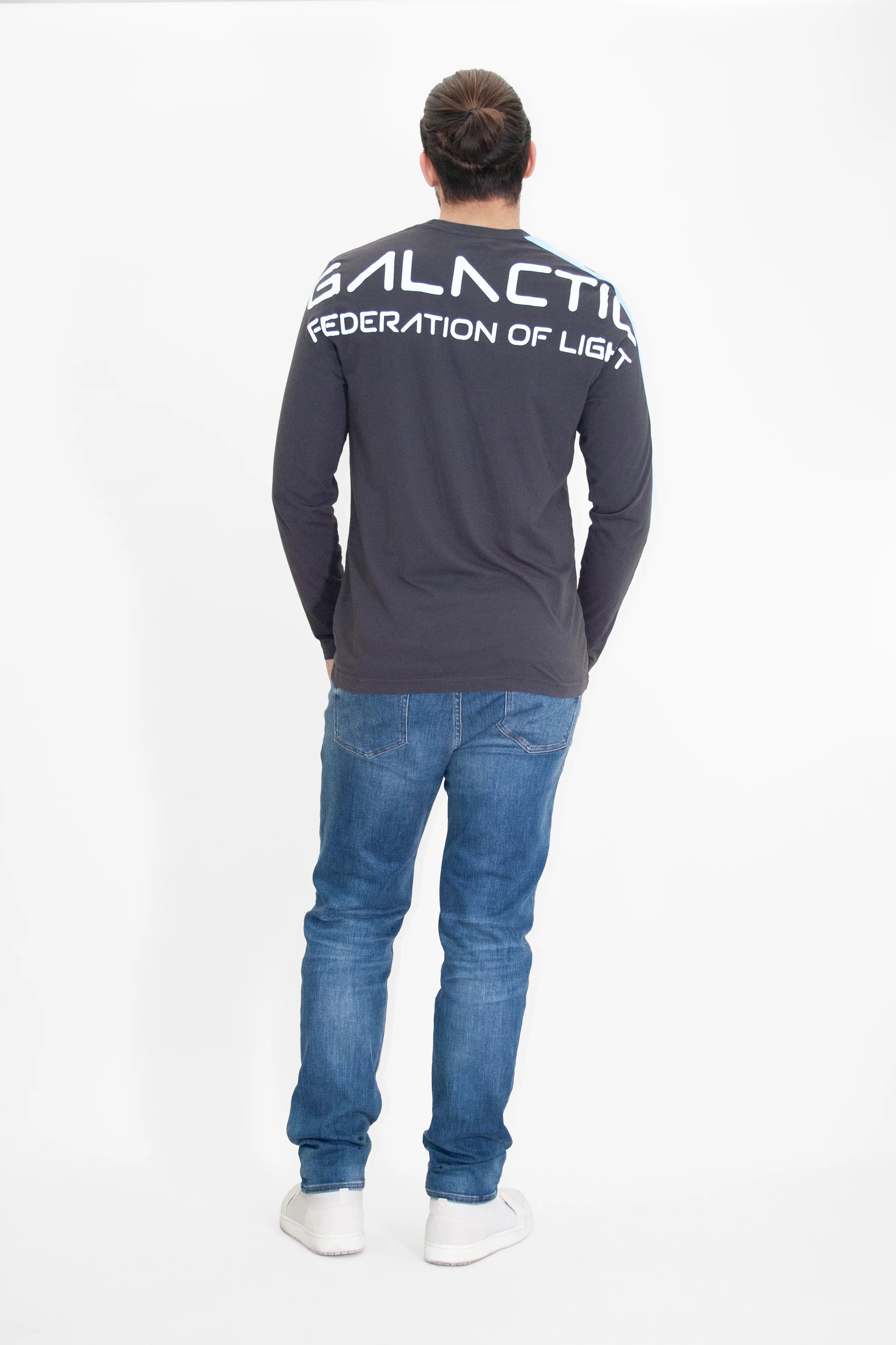 A person with a long ponytail stands facing away, wearing a dark GFLApparel GFL Stars L/S in Space Glow shirt made from breathable cotton with 