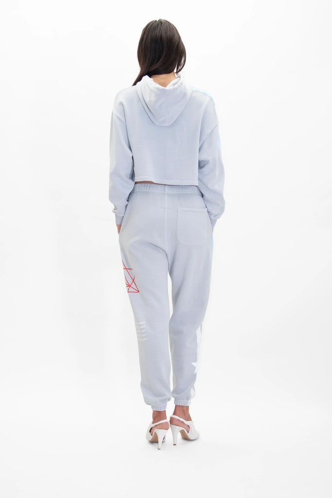 A person wearing a light blue cropped hoodie and GFLApparel Hypergalactic Pants in Galactic Gray with white high-heeled shoes, standing with their back to the camera. The jogger set features a drawstring waistband and is made from a comfortable heavyweight cotton blend.