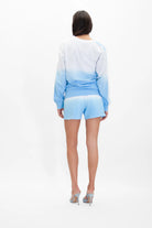 Person wearing the Illuminated Crewneck in Atmosphere by GFLApparel in a light blue and white gradient with matching shorts, standing with their back to the camera against a plain white background.