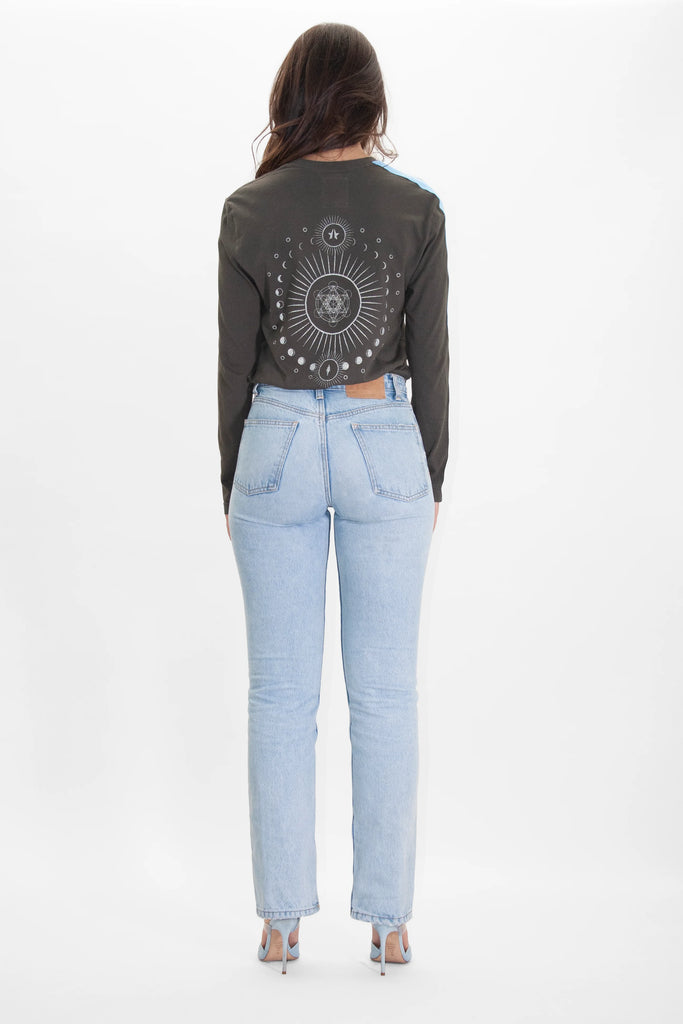 A person with long hair is standing facing away, wearing a long-sleeve cotton T-shirt featuring a Metatron design and light blue jeans, against a plain white background. They are wearing the Light Worker L/S in Caladan by GFLApparel.