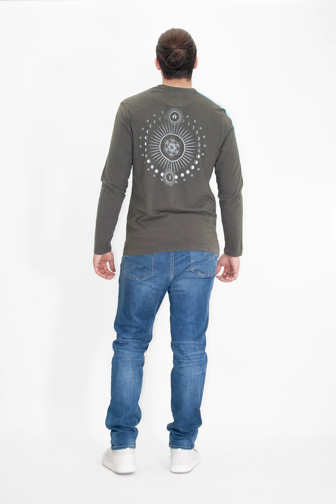 A person with long hair in a bun, wearing a Light Worker L/S in Caladan by GFLApparel with a Metatron design on the back, blue jeans, and white shoes, stands facing away from the camera against a white background.