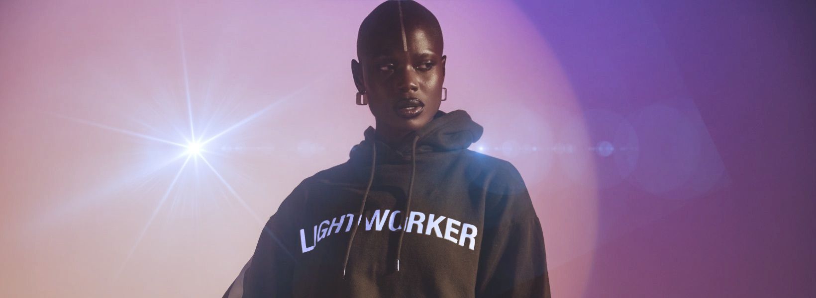 woman wearing a dark green hoodie with light worker emblazoned on the chest standing in front of a purple star background