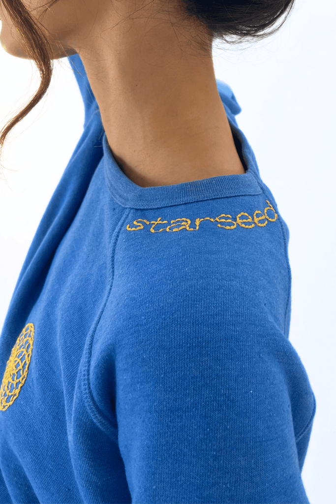 Close-up of a woman in a blue crewneck with the word "starseed" and the Lotus of Life Women's Crewneck embroidered in yellow on the collar, evoking spiritual symbolism from GFLApparel.