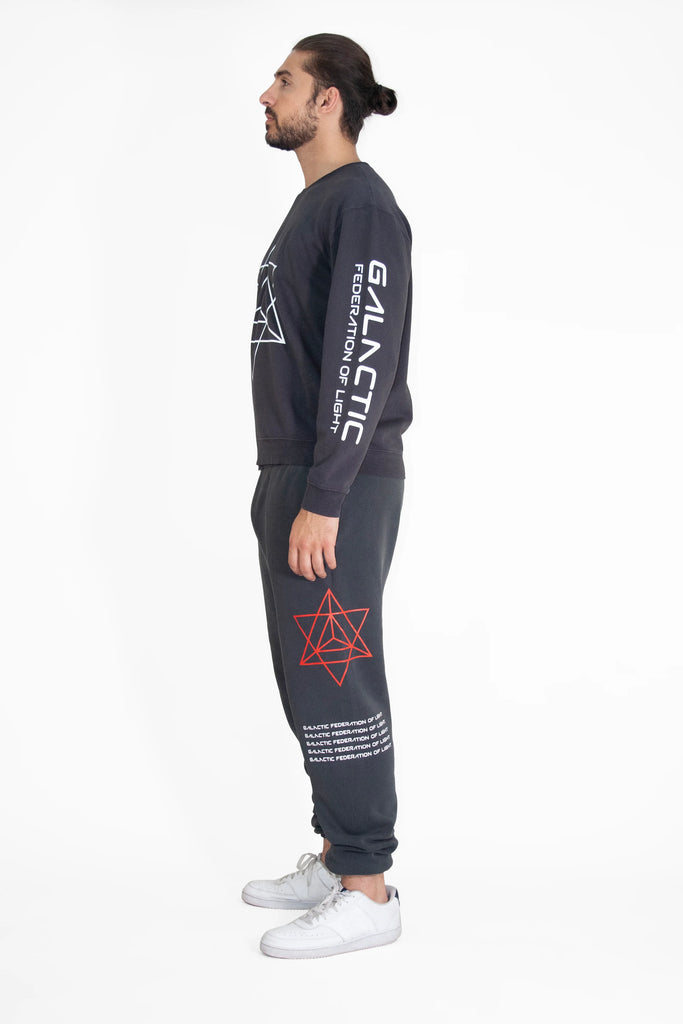 Side view of a person wearing a dark "Merkaba Crewneck in Space Glow" by GFLApparel, adorned with Sacred Geometry design and matching dark pants featuring a red star symbol and white text on the leg.