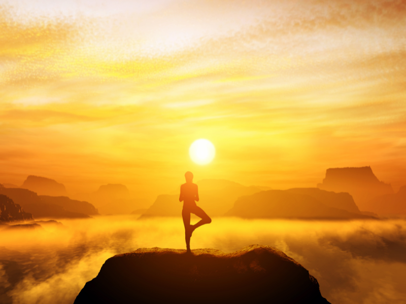 person doing yoga on mountaintop with a warm sunset in the back
