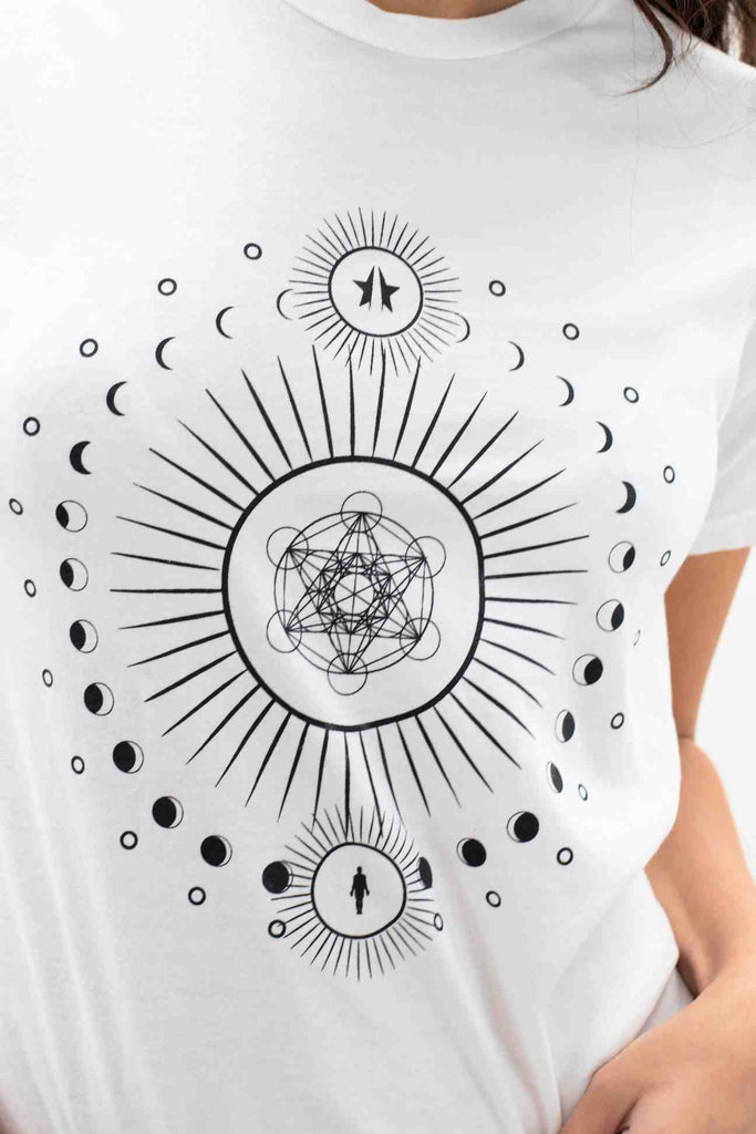 Woman wearing a white GFLApparel Moon Metatron Tee in Lite Beam with a black sacred geometry design featuring symbols like moons, stars, and circles.