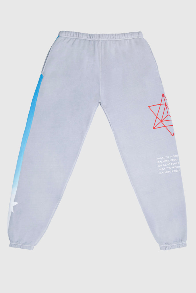 Introducing the Hypergalactic Pants in Galactic Gray by GFLApparel: a pair of light gray sweatpants crafted from heavyweight cotton blend, featuring a red geometric star on the right thigh and a blue gradient stripe down the left leg, complete with a comfortable drawstring waistband.