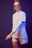 Person wearing a comfy GFLApparel More Light Tee in Nebula and matching shorts with white long sleeves and a collar under purple illumination.