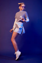 Person posing in a GFLApparel 369 Tee in Asteroid with sunglasses and white boots against a blue background.