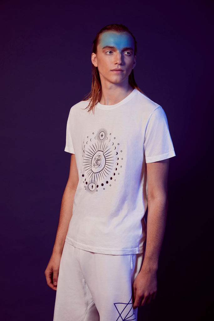 A person with long hair and blue face paint stands against a dark background, wearing the Moon Metatron Tee in Lite Beam by GFLApparel and white shorts.