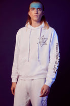 A person with long hair wears a Merkaba Hoodie in Lite Beam and matching sweatpants, both featuring sacred geometric designs and the text "Federation of Light" on the sleeve, against a purple background.