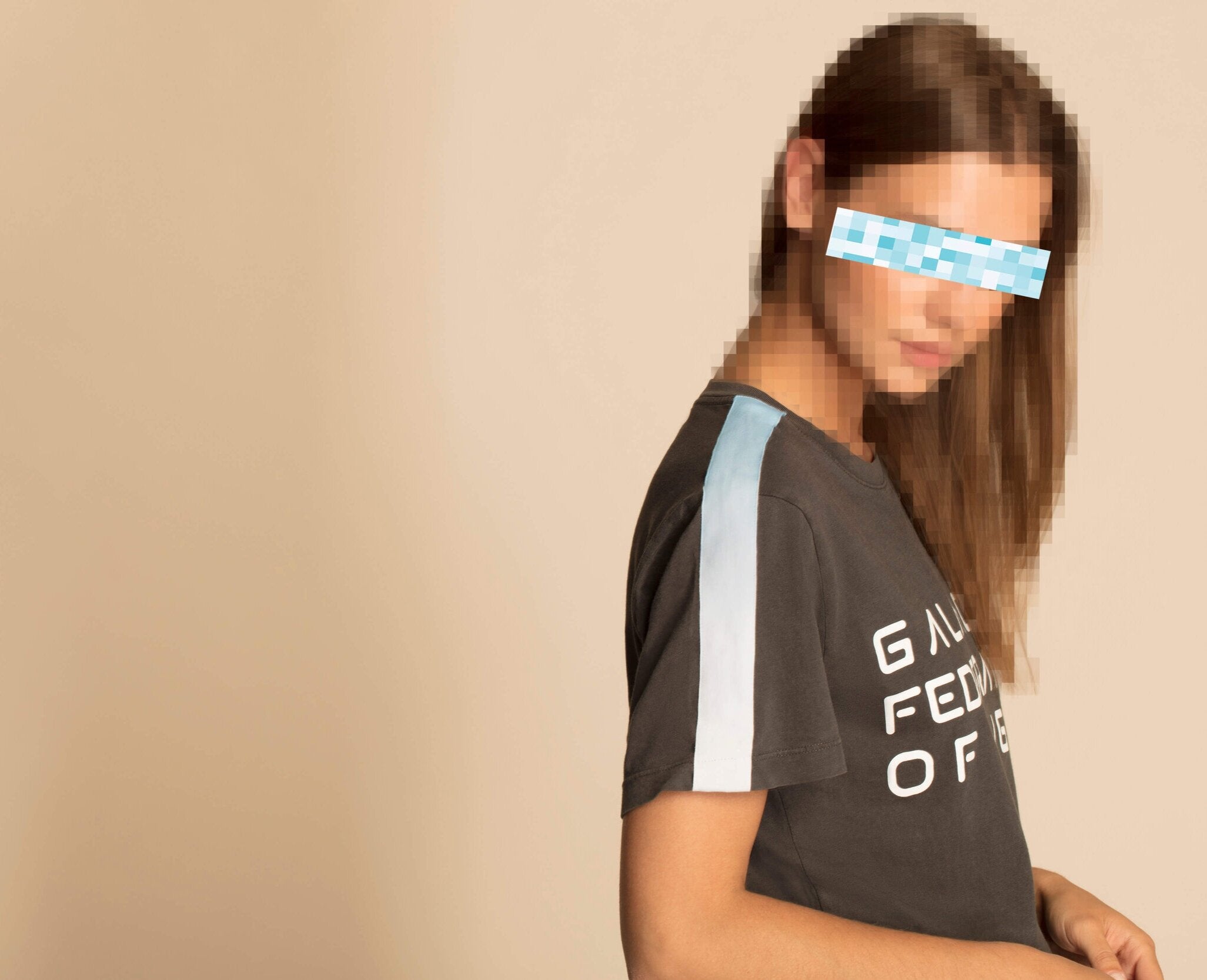 A person with long hair is wearing a GFLApparel GFL Stack Tee in Space Glow. The person's eyes are pixelated. The background is plain and neutral.