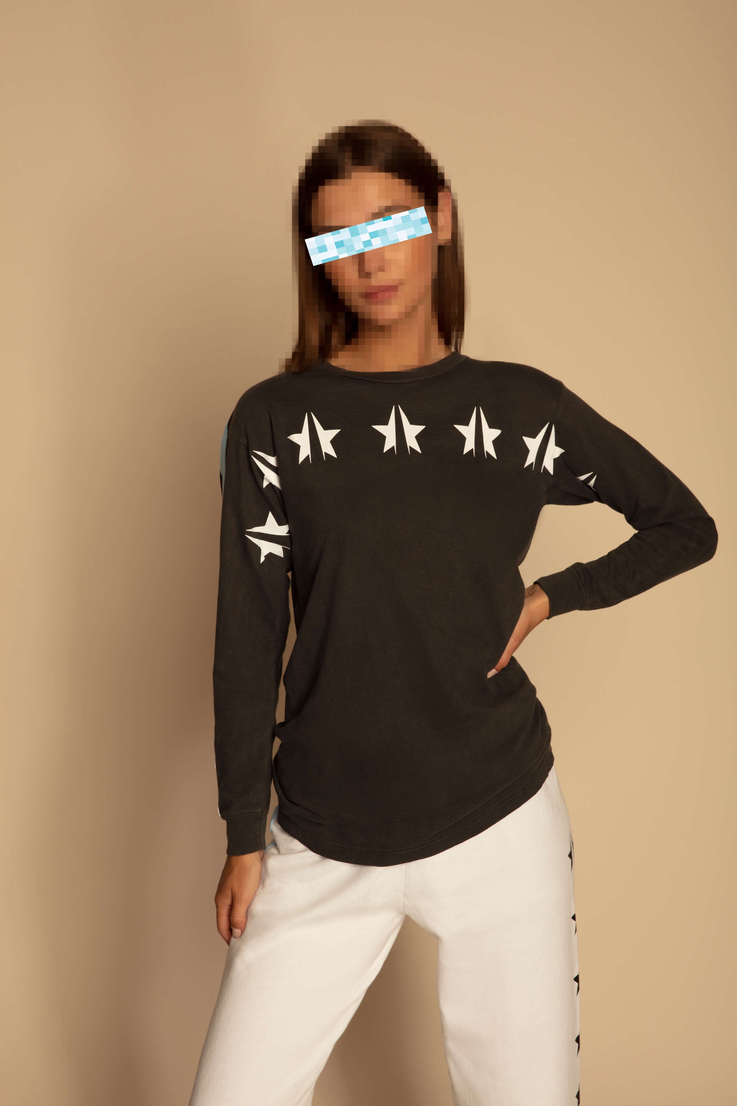 A woman stands in a relaxed pose, wearing a dark GFLApparel GFL Stars L/S in Space Glow with white airplane patterns and white pants made from breathable cotton. Her face is intentionally blurred.